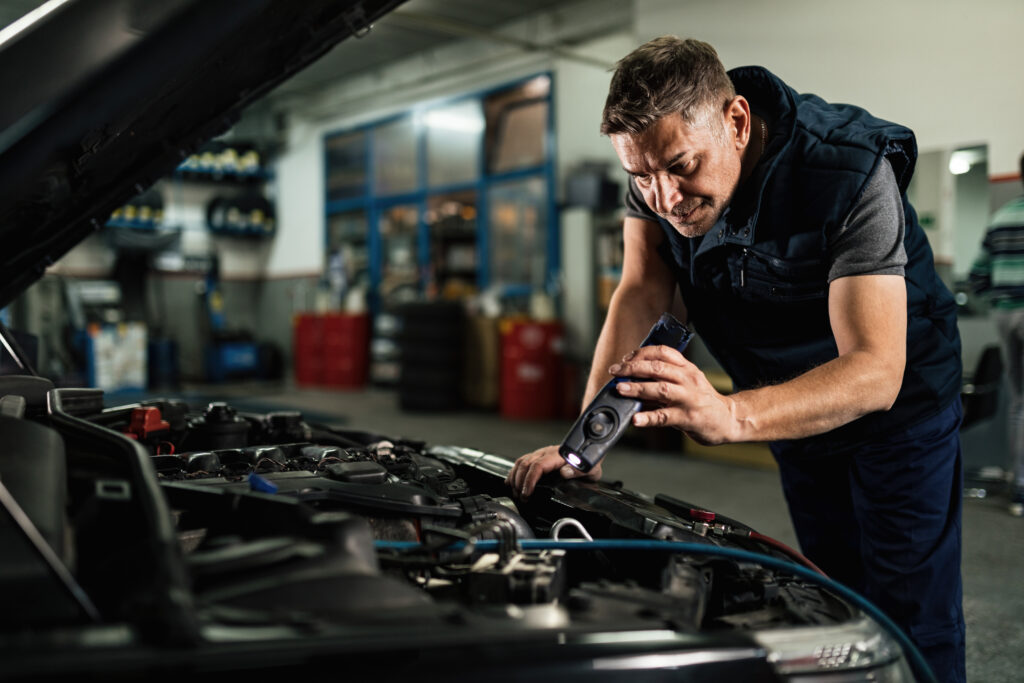 Auto mechanic using lap while examining car engine in repair sho